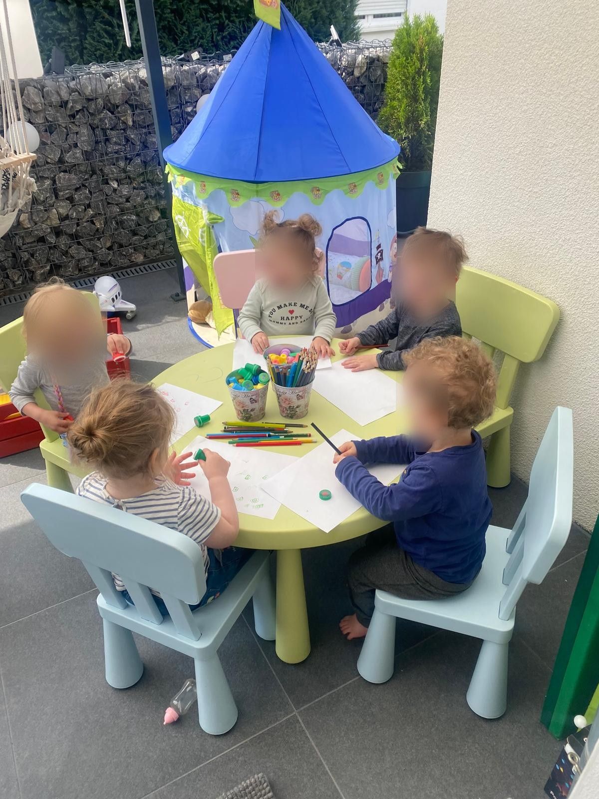 Kinder malen gemeinsam am Kindertisch auf der Terrasse
